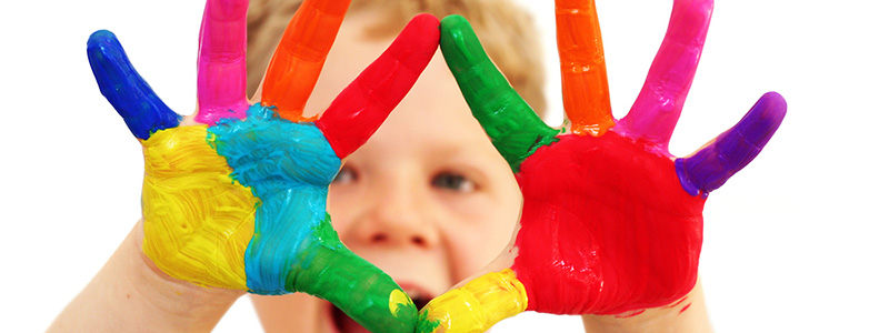 Child holding up hands covered in bright paint, representing creative activities in the church’s children’s ministry.