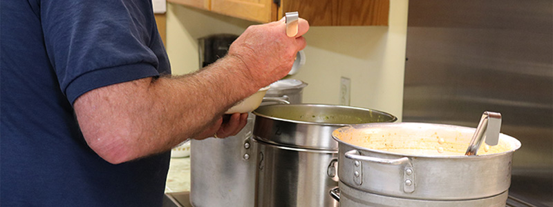 Volunteer serving soup from large pots in a community kitchen.